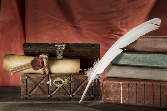 Vintage still life. Feather near sealed scroll in old chest and vintage books on red background