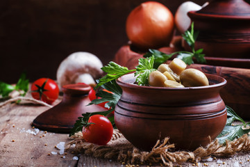 Marinated mushrooms champignons in a clay pot, vintage wooden ba