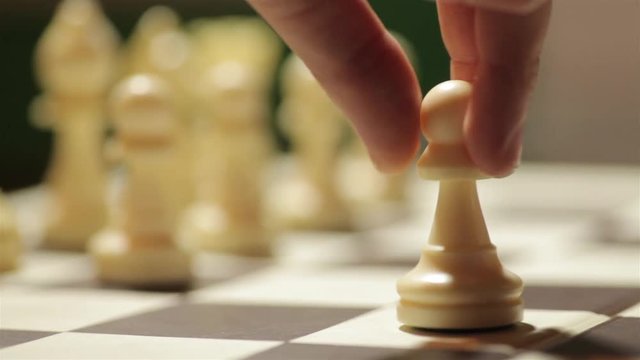 Panning shot of a chess board with a hand moving the white pawn.