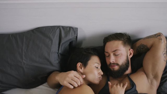 4K Camera tilts down to find a couple in bed talking and laughing before sharing a kiss