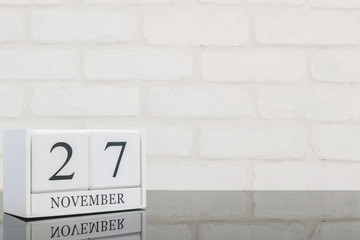 Closeup white wooden calendar with black 27 november word on black glass table and white brick wall textured background with copy space , selective focus at the calendar