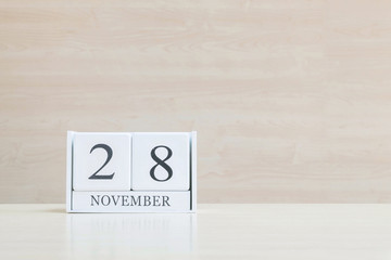 Closeup surface white wooden calendar with black 28 november word on blurred brown wood desk and wood wall textured background with copy space , selective focus at the calendar