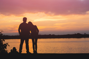 Silhouette of loving couple standing riverside and beautiful sunset background.