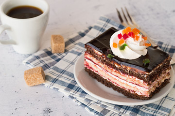  Chocolate cake.  Chocolate cake with cream on a plate, coffee cup, a fork and two pieces of sugar on a light table.