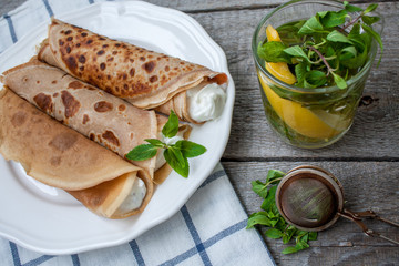 Russian thin pancakes with butter, cheese, jam, mint on a napkin on a wooden background.  Love for a healthy sweet  food concept