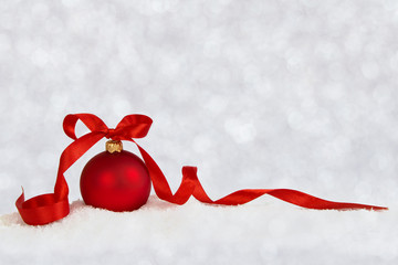 Christmas ball with red ribbon on artificial snow flakes. Defocused background.