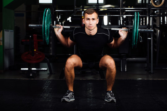 Man training squats with barbells over head.