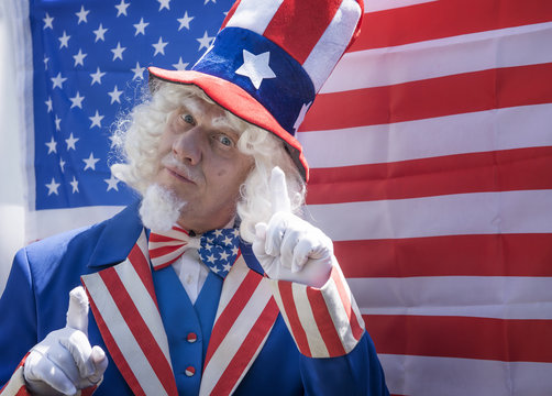Portrait image of a man dressed a Uncle Sam. Standing in front of an American Flag.