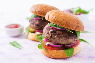 Big sandwich - hamburger burger with beef, pickles, tomato and red onions on a light background.