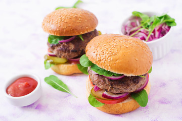 Big sandwich - hamburger burger with beef, pickles, tomato and red onions on a light background.