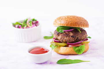 Big sandwich - hamburger burger with beef, pickles, tomato and red onions on a light background.