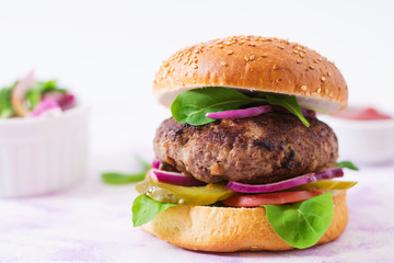 Big sandwich - hamburger burger with beef, pickles, tomato and red onions on a light background.