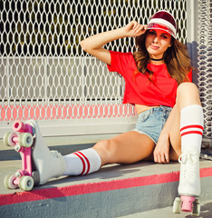 Pretty brunette girl in a red top and jeans shorts, red sunvisor and vintage roller derby has a...