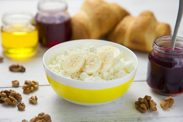healthy breakfast - crumbly, cottage cheese with banana, walnuts, croissants, honey and lingonberry jam in a bowl standing on  wooden table