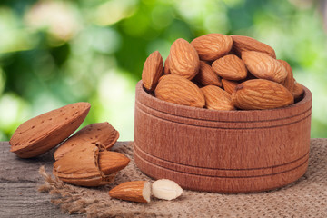 almonds in a bowl on the old wooden board with sackcloth and blurred garden background