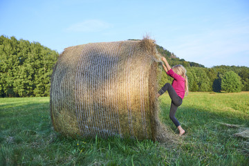 Naklejka na ściany i meble Child blond Girl by straw hay bale in field, meadow, playing, children summer activities