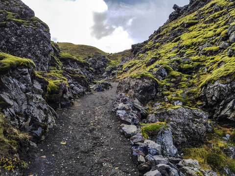 Hiking through the lava field of Laugahraun, Landmannalaugar, Iceland. Moss covered rocks are shining in the sunlight under a moody sky