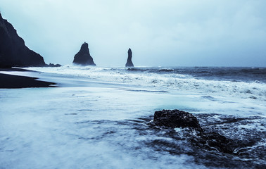 Rock formation on black volcanic beach at Cape Dyrholaey, South Iceland, with mount Reynisfjall on the background