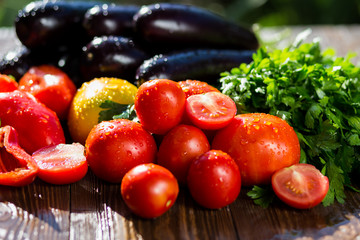 Close-up of fresh, ripe tomatoes, eggplant, sweet red pepper and parsley on wood background.Group of vegetables. Red and yellow tomatoes,pepper, eggplant and parsley in drops of water 