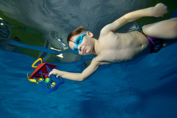 Happy little boy swimming underwater in the pool with a Christmas toy in hand. Portrait. The view from under the water at the bottom. Landscape orientation © alexbard