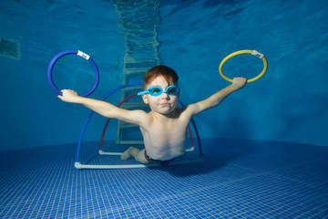 Little boy swims under water and trains in the pool with rings and hoops. Portrait. Close-up. The view underwater. Landscape orientation © alexbard