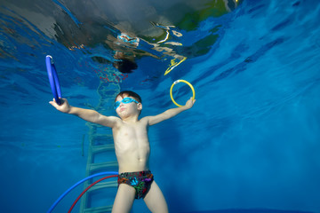 Little boy underwater in the pool, swims and trains with the rings. Portrait. Shooting underwater. Landscape orientation © alexbard