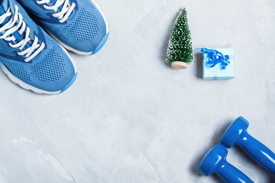 Christmas sport composition with shoes, dumbbells and blue gift
