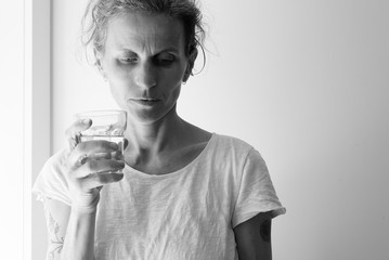 Middle aged woman holding glass and looking pensive - addiction concept (black and white)