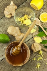 Preparing ginger tea against influenza. Traditional treatment for colds. Ginger, lemon and honey bowl on wooden table. Rustic wooden background. Home Pharmacy.
