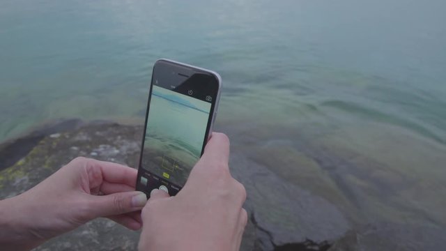 Young woman takes photographs of Lake Geneva using her smartphone camera. Close up on hands and phone.