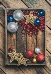 Christmas or New Year holiday decoration background. Christmas tree glittering toy stars, balls and garland in wooden box over rustic wooden background, top view, copy space, vertical composition