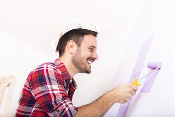 Young smilling man painting wall in their new house. Home, moving, painting and renovating concept
