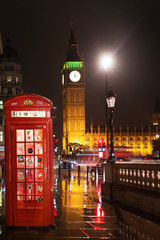 Popular tourist Big Ben and Houses of Parliament with red phone booth in night lights illumination in London, England, United Kingdom