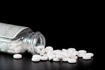 Spilled aspirin bottle on black reflective surface. Aspirin tablets are spilling from the mouth of...