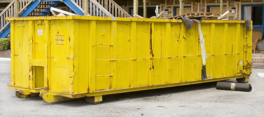Huge yellow industrial dumpster full of construction and renovation debris in motel parking lot....