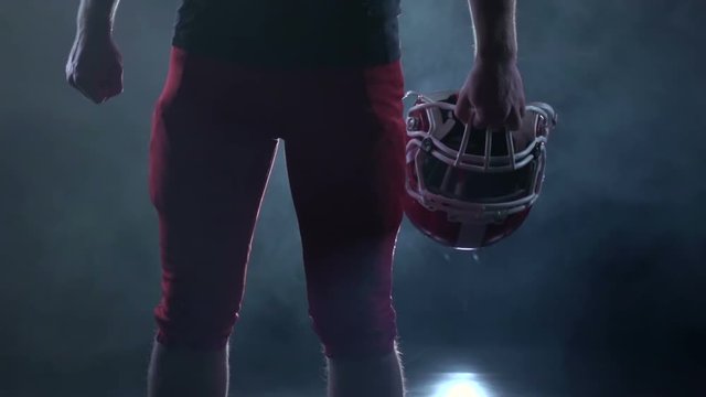 Football player holding a red protective helmet. Black background. Slow motion