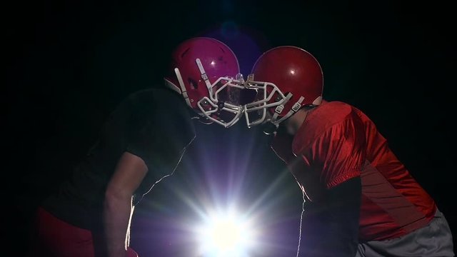 Two male footballer face their protective helmets. Black background. Slow motion
