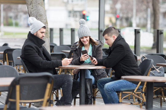Three young friends sitting in a coffee shop and using smartphones..