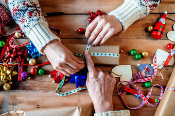 Hands of two women wrapping Christmas gifts.