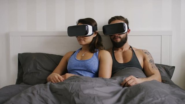 4K Young couple in bed using virtual reality headsets