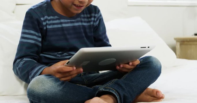 Boy using digital tablet while relaxing on bed
