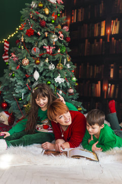 Mother With Her Kids Reading The Book Near Dressed Up Christmas Tree