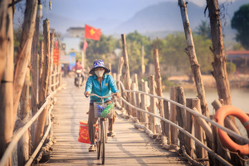 Vietnamese woman rides a bicycle by the wooden bridge with vietnam flag on  background
