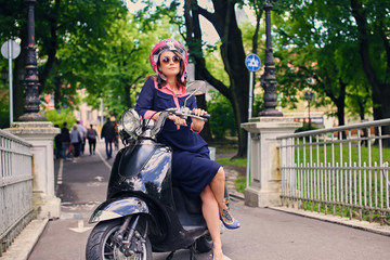 Fototapeta na wymiar A woman in a dress sits on a moto scooter.
