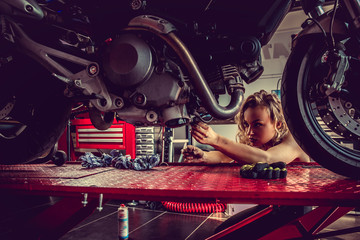 Fototapeta na wymiar Blonde female repairing motorcycle in a garage.