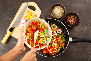 Woman putting chopped bell pepper with onion in pan, top view