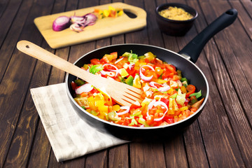 Frying pan with chopped bell pepper and onion on wooden background