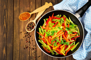 Frying pan with chopped bell pepper and spices on wooden background, top view