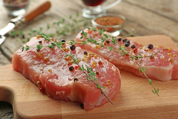 Steaks in marinade with thyme and garlic on wooden board