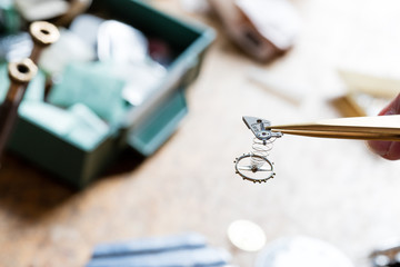 closeup of tweezers pinching a little spring or clockwork in a watchmaker workshop
